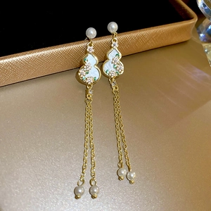 Detail of gold gourd earrings with flower enamel and dangling pearls on jewelry box