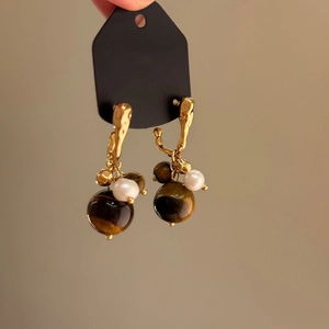 Detail shot of golden drop earrings with brown tiger-eye beads and white pearls