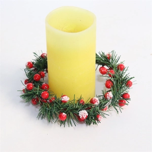 Detail of yellow pillar candle with Christmas wreath of red berries and green leaves