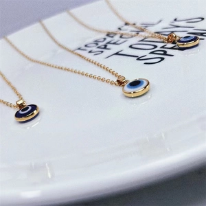 Three gold stainless steel evil eye pendant necklaces displayed on a white ceramic plate