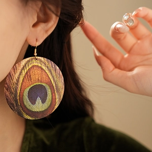Macro view of round peacock feather pattern earring worn on model's ear with gold hook