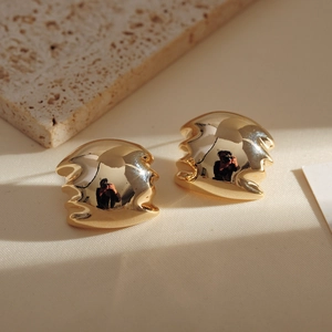 Detail of gold-plated geometric drop earrings on natural stone surface with soft lighting