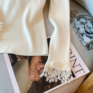 Vue détaillée du pull en maille crème avec poignets en dentelle florale et côtes