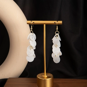 Detail view of long shell tassel earrings with white circular sequins on a golden stand