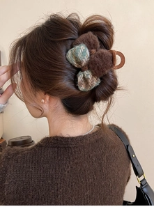 Detail view of tweed bow hair claw clip with plush pom poms on model's hair