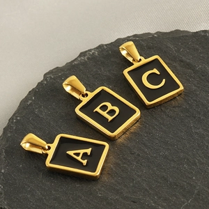 Golden square alphabet pendants with A, B, and C initials on a natural slate stone