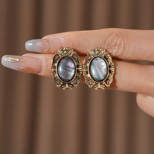 Macro view of vintage gold-tone resin oval studs with ornate floral border held by hand