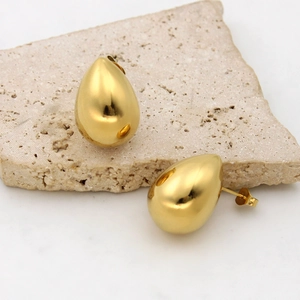 Close-up of polished gold-plated stainless steel teardrop earrings on a beige stone