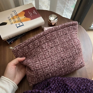 Detail of hand-held woven tweed cosmetic bag in dusty pink and purple textured knit
