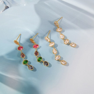 Detail of elegant gold-plated drop earrings featuring colorful zircons on a blue background