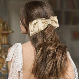 Detail of elegant champagne satin bow hair clip styled on model's hair in a back view