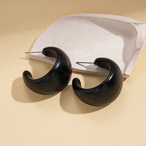 Detail of matte black acrylic C-shape hoop earrings on a minimalist ceramic prop