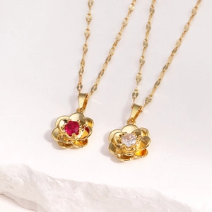 Classic rose pendant necklace in gold with red and white gemstones on stone surface