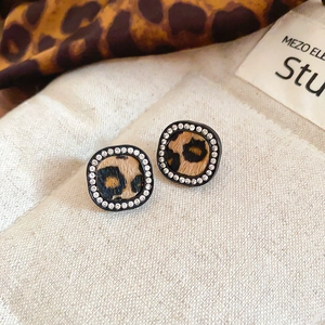 Macro shot of square leopard print earrings with sparkling rhinestones on beige fabric