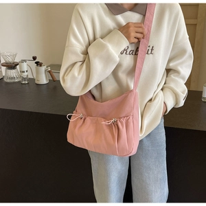 Detailed view of pink pleated nylon crossbody bag styled with a white sweater in a cafe