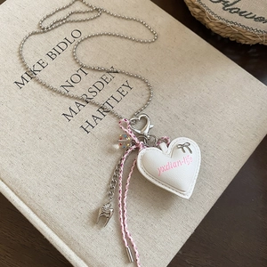 Detail of pink cotton cord necklace with heart pendant and silver bow on book