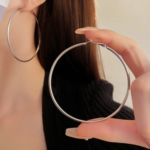 Close-up of a model wearing large silver hoop earrings with a minimalist metal design