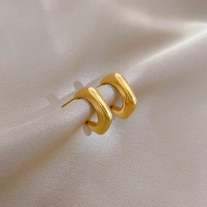 Macro shot of thick gold C-shaped titanium earrings on elegant pleated champagne silk fabric