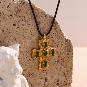 Detailed close-up of 18K gold-plated cross pendant with green gems on a textured rock
