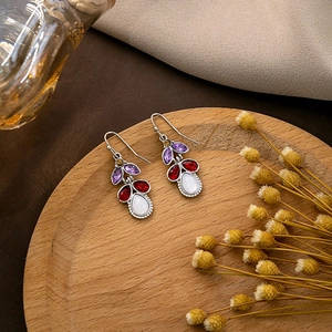 Retro bohemian drop earrings with purple and red gems on a rustic wooden display