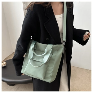 Detailed view of light green nylon tote bag worn over a black coat with shoulder strap