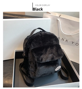 Detalle de mochila de felpa negra con bolsillo frontal y etiqueta en caja de regalo