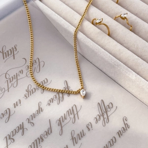Detail view of gold necklace with teardrop pendant and matching rings in a gift box