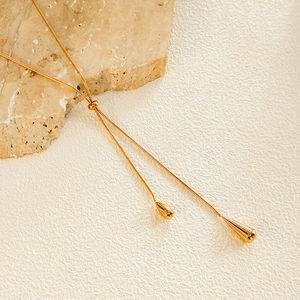 Detailed view of golden snake chain necklace with dual teardrop pendants on a stone surface