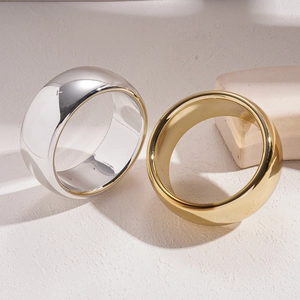 Minimalist wide band rings in polished gold and silver finishes on stone background