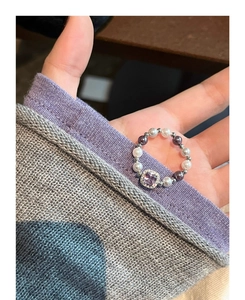 Detail of square purple gemstone ring with alternating white and dark pearls on hand