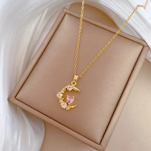 Close-up of golden moon pendant with pink heart zircon and crystals on beige jewelry box