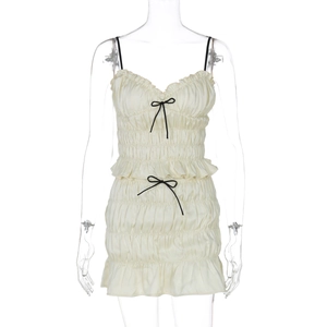 Detail of off-white pleated mini dress featuring delicate black bow ties and ruffled hemline