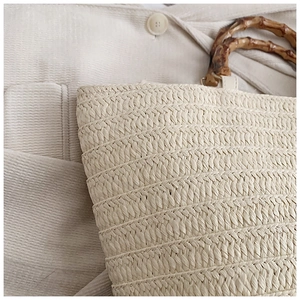 Detail of straw tote bag featuring natural woven texture and vintage bamboo handles