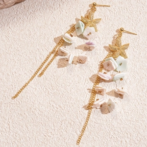 Starfish seashell fringe drop earrings in gold metal on a textured beige surface