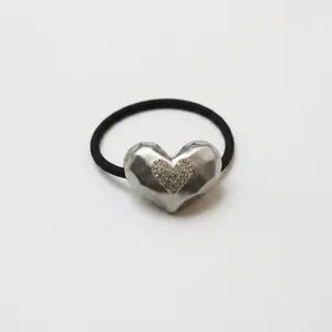 Detailed view of black elastic hair tie with a brushed silver heart-shaped metal charm