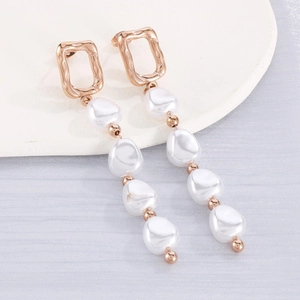 Détail de boucles d'oreilles géométriques en or rose avec quatre perles baroques blanches