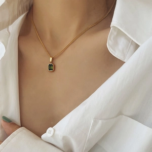 Vintage gold necklace with emerald pendant worn by a model on a white shirt background