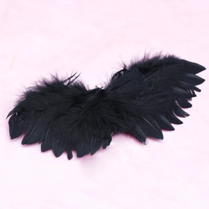 Detail view of black feather wings accessory for dolls on a pink fabric background
