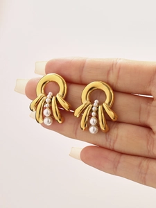 Detail of layered gold stainless steel earrings with four white pearls held in hand