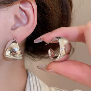 Detail of glossy silver C-shaped chunky hoop earrings showing polished metallic texture