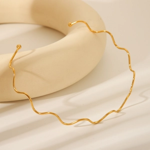 Macro shot of a wavy gold stainless steel choker collar on a minimalist beige display stand