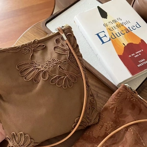 Détail des broderies florales sur le sac à bandoulière en daim marron sur une table en bois