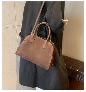 Detailed side view of a brown suede tote bag carried by a model in a modern interior