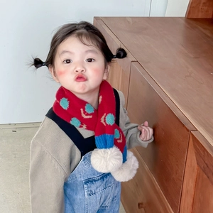 Close-up of a red knitted toddler scarf with floral patterns and soft white pom-poms