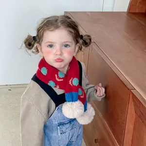 Dettaglio di una sciarpa in maglia rossa per bambini con motivi floreali e pompon bianchi
