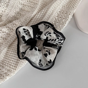 Detailed close-up of a floral silk scrunchie with black edging on a white surface