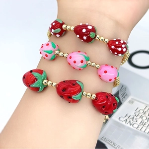 Detailed view of beaded bracelets featuring red and pink strawberry charms with gold beads