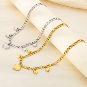 Close-up of gold and silver heart necklaces with Cuban links on silk fabric