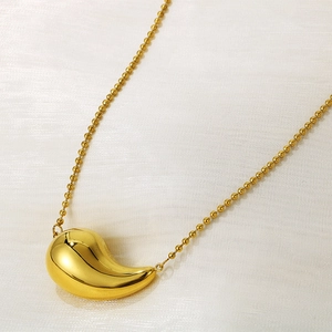 Gros plan d'un pendentif goutte doré poli sur une chaîne à billes et tissu doux