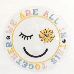 Detail of round suncatcher sticker featuring embroidery text WE ARE ALL IN THIS TOGETHER